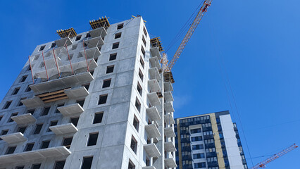 Construction crane against the background of a concrete slab house under construction. Construction of an apartment building.