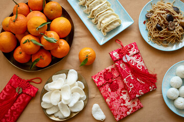 Chinese New Year food on a table with dumplings, noodles, oranges with red envelopes for gifts
