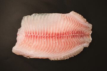 Fresh tilapia fillet on black background, top view.
