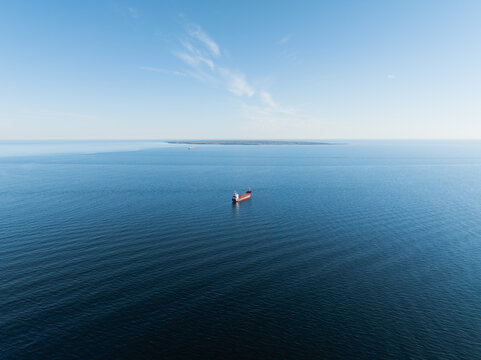 A cargo ship sails through the calm waters of the Baltic Sea under a clear sky, bird's-eye view.