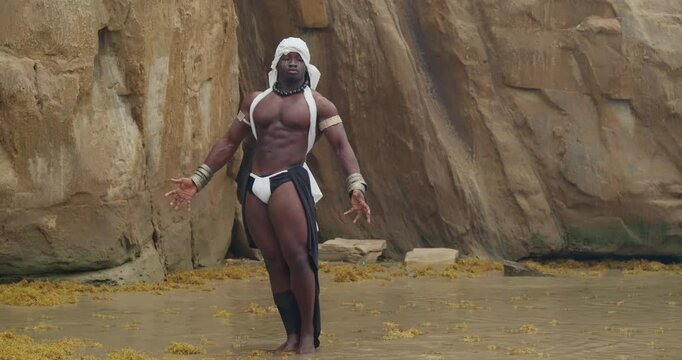 A beach is the setting for this muscular, dark-skinned male cosplayer.