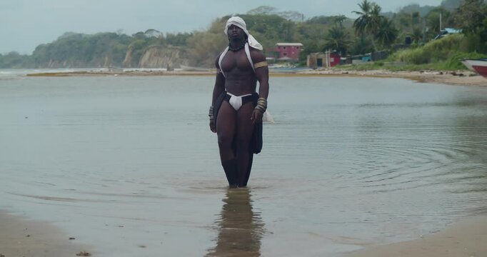 Beach scene: a dark-skinned male cosplayer displaying muscles.