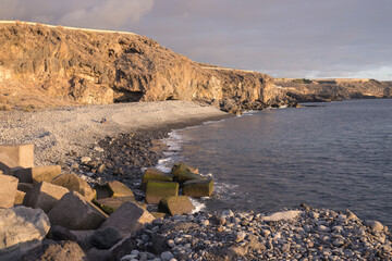 Picturesque rocky pebbles beach with stones wall in Playa de San Juan. Playa de San Juan is a small fishing village on the south west of Tenerife island. Golden hour light