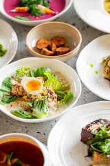 A top-view shot of variety of colorful and appetizing dishes on dining table, including salad with a soft-boiled egg, roasted vegetables, soup, and other gourmet meals, highlighting fresh ingredients
