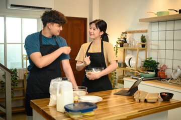 Man and woman wearing aprons mixing ingredients for pancakes in a cozy kitchen
