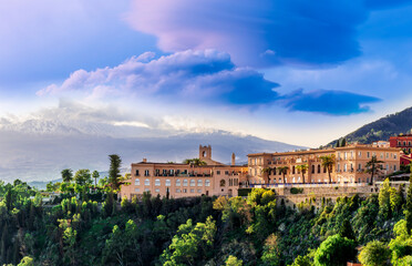 Fototapeta premium Amazing landscape of a beautiful mountain town Taormina in Sicily, Italy. Scenic view from a green mountain to a beautiful famous hotel and high majestic mount vulcan Enta in snow.