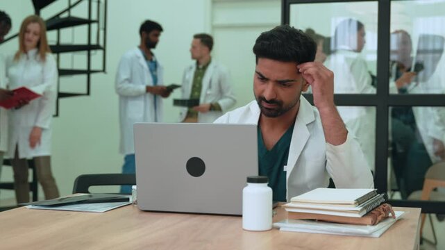 Healthcare indian worker studying patient files on laptop, focusing intently while working in contemporary clinical setting, displaying professional concentration