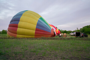 Obraz premium Colorful aerostat balloons are being inflated on the ground, ready for an upcoming flight in a rural area under a cloudy sky.