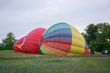 Obraz premium Colorful aerostat balloons are being inflated on the ground, ready for an upcoming flight in a rural area under a cloudy sky.