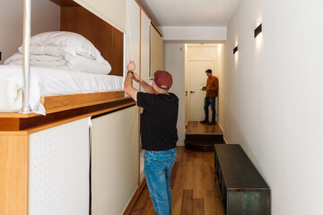 Modern hostel with cozy minimalist dorms, wooden capsule beds, and peaceful courtyard. Men chatting...