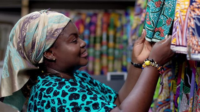 Smiling African woman, successful small business owner of an African Print, Ankara fabric shop proudly displaying textiles prints.