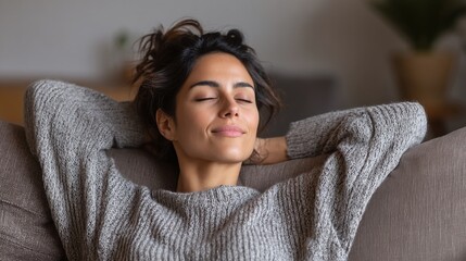 Relaxing woman: A woman with dark hair is reclining with her hands behind her head. She has a soft smile as she rests on a couch.