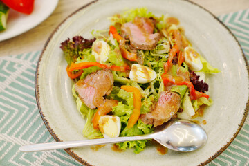 A plate of meat salad made from lettuce, quail egg, vegetables and steak.