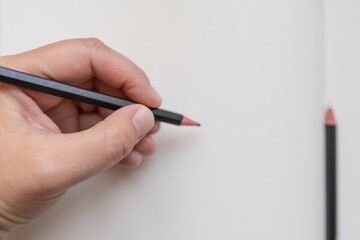A hand holding a black wooden pencil, ready to draw on blank white paper. Concept of creativity, inspiration, and starting a new artistic journey