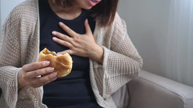 Asian woman suffering from heartburn and indigestion after eating fast food like burgers, feeling discomfort with chest pain and stomach ache, possibly caused by acid reflux or GERD