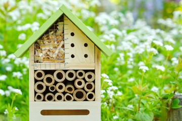 An insect hotel or bee hotel in a summer garden with flowers. An insect hotel is a manmade structure created to provide shelter for insects in a variety of shapes and sizes and materials.	