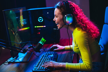 Young woman streaming video games in vibrant neon lit room with a professional gaming setup and colorful headset