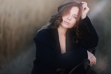 A female model poses sitting on a chair among nature and fields, an unusual photo of a summer Look