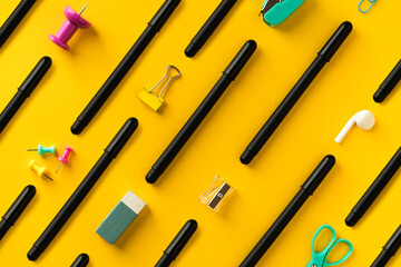 School supplies and black pens flat lay on yellow background