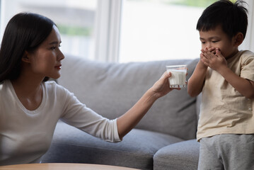 Adorable Asian baby boy using hands closing his mouth sign for refuse drinking cow milk from his mother. Kids food nutrition no appetite, food aversion or picky eating behavior food rejection concept.
