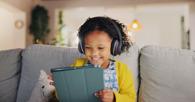 Tablet, headphones and happy child on sofa for music, online learning and play game for education. Girl, audio and kid with tech in home living room for internet app, streaming cartoon or watch video