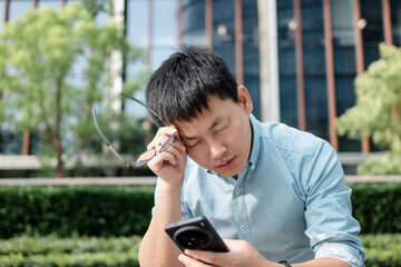 asian man headache while using smart phone outdoor
