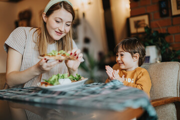 A warm indoor moment depicting a mother sharing joy and food with her child in a cozy home environment.