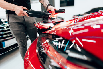 Professional car detailer using an orbital polisher to polish the hood of a red car, ensuring a smooth and shiny finish in a modern auto detailing shop