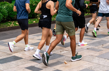 Urban running club community in colorful activewear jogging together across pedestrian areas, bridges, and parks. Anonymous group of runners in a vibrant city setting