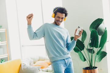Young man wearing headphones enjoying music and dancing at home in a stylish living room with bright natural daylight