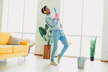 Young man enjoying cleaning while grooving to music in a stylish living room filled with natural light and cozy decor