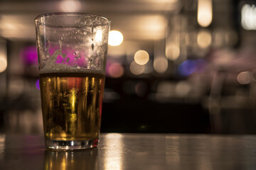 Cold beer glass sitting on bar with blurred background