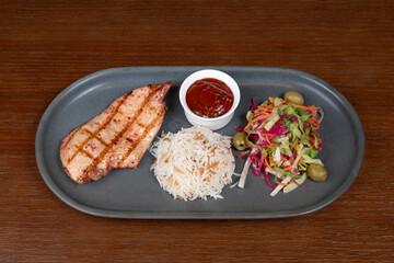 Grilled chicken steak with tomato sauce, Turkish rice, adjika and mixed salad with lemon on a plate
