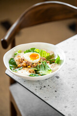 fresh homemade salad with lettuce, corn, tuna, and a boiled egg with a runny yolk, served in a white bowl and garnished with creamy dressing and seasoning on a speckled countertop