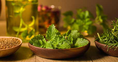Mint, rosemary, and coriander seeds are placed in wooden bowls with traditional Chinese medicine concepts. Behind is a blurred image of glass jars, containing essences and dry ingredients.