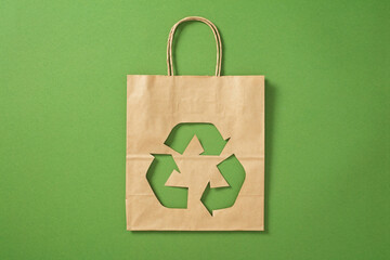 Brown paper bag with cutout recycle symbol on green background. Eco-friendly shopping, zero waste concept.