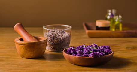 Deep purple lavender flowers are placed in a wooden bowl, next to crushed flower buds placed in a glass bowl. The lavender will be crushed by hand with a mortar and pestle. Natural herbs medicine.