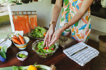 Woman preparing a fresh vegetable salad with lime dressing on a jungle veranda in Sri Lanka. Tropical lifestyle, healthy eating, and colourful ingredients in natural surroundings