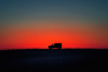 Fototapeta premium Truck driving through a sunlit field at sunset.