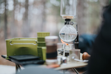 Innovative siphon coffee apparatus prepared outdoors, surrounded by rustic winter nature for a mountain picnic.