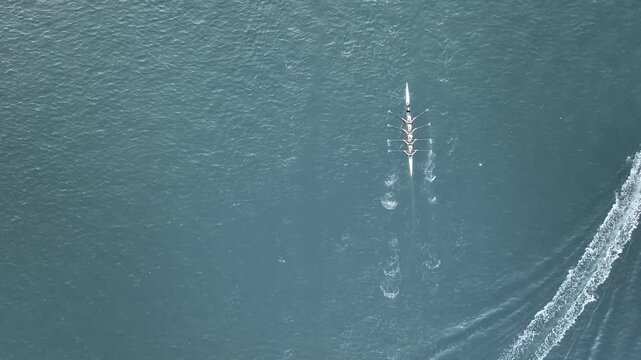 Tracking Aerial shot of rowers rowing down a river past boats.