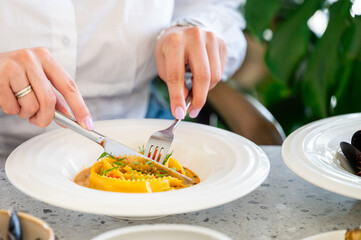 person dining at a restaurant enjoys a plate of ravioli in a creamy sauce, elegantly presented with fresh herbs. The close-up highlights the vibrant colors and gourmet quality.