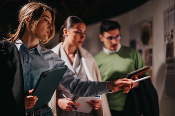 A group people attentively examines exhibits in a museum, discussing and analyzing the displays,...