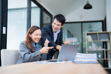 Two happy asian business partners celebrating successful project while working together on laptop in modern office, expressing excitement and joy