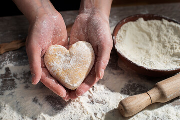 Baking concept. Caucasian female hands holding heart shaped dough.