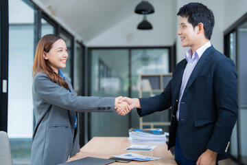 Fototapeta premium Two asian businesspeople in suits shaking hands after reaching an agreement during a meeting in a modern office, showing trust and cooperation