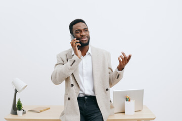 Confident man talking on mobile phone while standing at modern office desk against white...