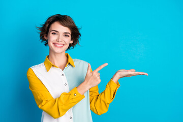 Fototapeta na wymiar Photo of cheerful sales manager smile girl in stylish shirt pointing finger hold promo ad on arm isolated over blue color background