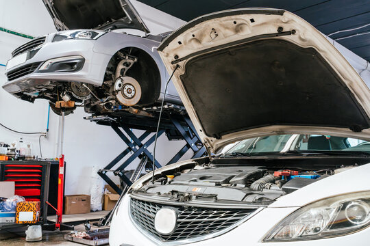 Two cars getting fixed in auto repair shop with open hoods