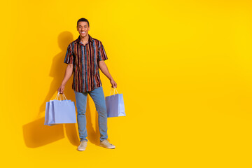 Young stylish man holding shopping bags with a bright yellow background showcasing modern fashion...